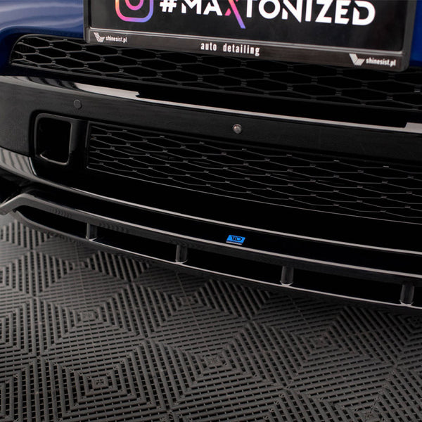 Car front bumper exhibits a black grille. A license area displays text: "#MAXTONIZED / auto detailing / shinesist.pl." The vehicle rests on a patterned, gray flooring.