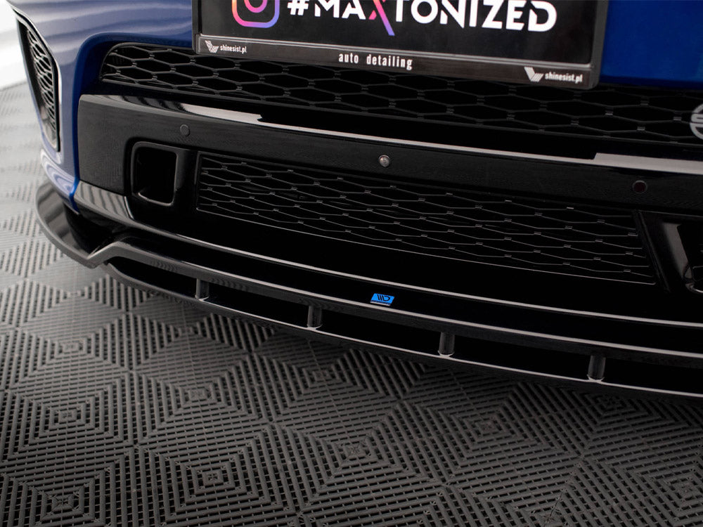 Car front bumper exhibits a black grille. A license area displays text: "#MAXTONIZED / auto detailing / shinesist.pl." The vehicle rests on a patterned, gray flooring.