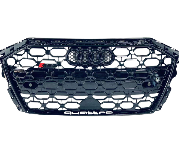 A black honeycomb car grille displays the Audi rings logo at the center and "quattro" text at the bottom. It features a small "RS" badge on the left.