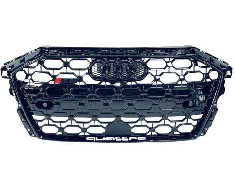 A black honeycomb car grille displays the Audi rings logo at the center and "quattro" text at the bottom. It features a small "RS" badge on the left.