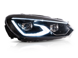 A car headlight displaying illuminated LED lights is positioned in a bright studio setting with reflections visible on its clear surface.