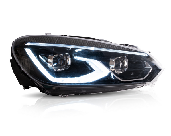 A car headlight displaying illuminated LED lights is positioned in a bright studio setting with reflections visible on its clear surface.