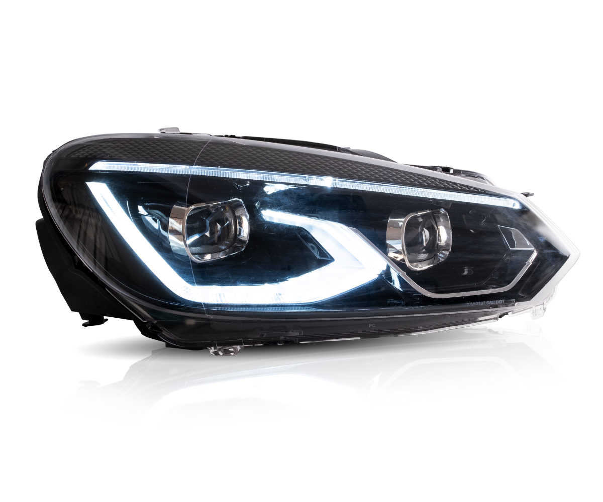 A car headlight displaying illuminated LED lights is positioned in a bright studio setting with reflections visible on its clear surface.