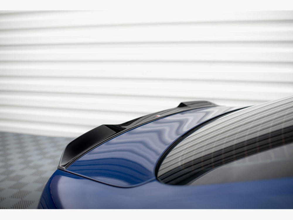 A sleek, blue car with a black spoiler rests on a textured surface, with a corrugated metal wall in the background reflecting on the rear window.