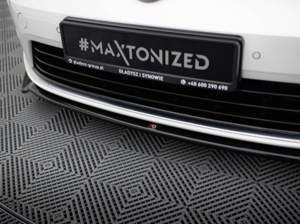 Car bumper displayed with a "#MAXTONIZED" plate attached above a mesh floor. Additional text includes "gladysz-group.pl," "GLADYSZ I SYNOWIE," and "+48 600 290 690."