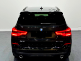 A black BMW X3 is parked indoors, with bright red taillights illuminated. The model designation 