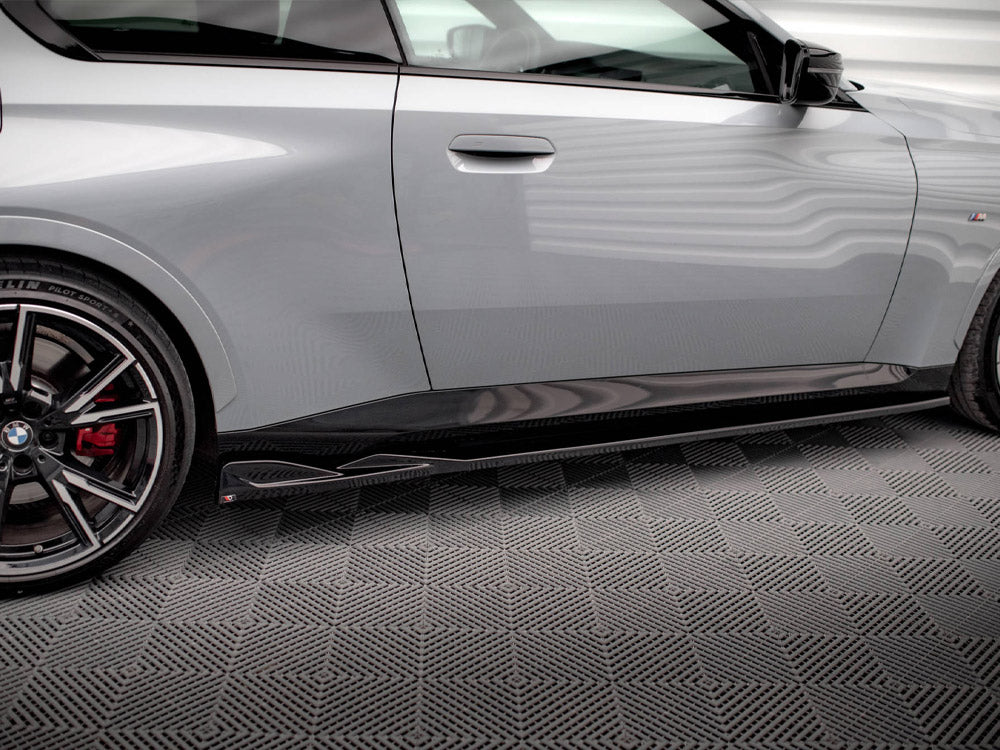 A sleek gray car with a visible wheel and side skirt detail is parked indoors on a textured floor. Brand and model emblems are visible.