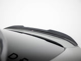 A black car roof spoiler is mounted on a smooth, grey vehicle surface. Partial letters 