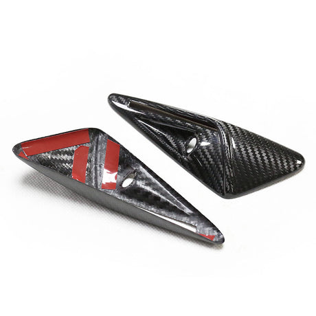 Two triangular carbon fiber pieces are positioned on a white surface. One piece has red adhesive strips and a circular hole, indicating they may be mounting components.