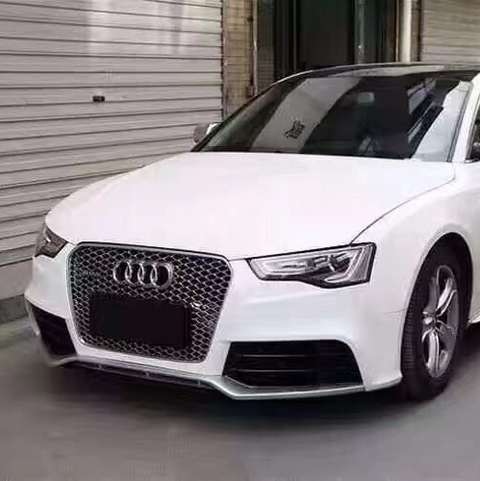 A white Audi car is parked in a garage with metallic shutter doors. The car features a prominent front grille and sleek design, positioned near the entrance of a building.
