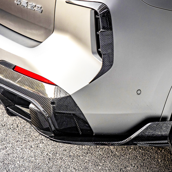 A car's rear bumper with carbon fiber details and a visible tire is parked on an asphalt surface. There is text in Chinese on the bumper.