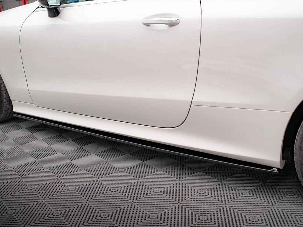 A white car is parked in a garage on a textured gray floor. The focus is on the side view, showing part of the front and rear tires.