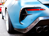 A blue sports car's rear features chrome exhausts and red tail lights, parked on a city street with another car partially visible in the background.
