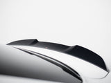 A black car spoiler is mounted on a sleek, white vehicle in a minimalistic setting. The background is a plain, light gray color, emphasizing the spoiler's contours.