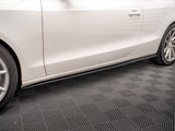 A white car with sleek design features rests on a textured garage floor, showcasing its side profile with visible wheel rims and a door handle.