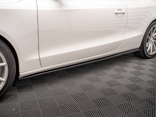 A white car with sleek design features rests on a textured garage floor, showcasing its side profile with visible wheel rims and a door handle.