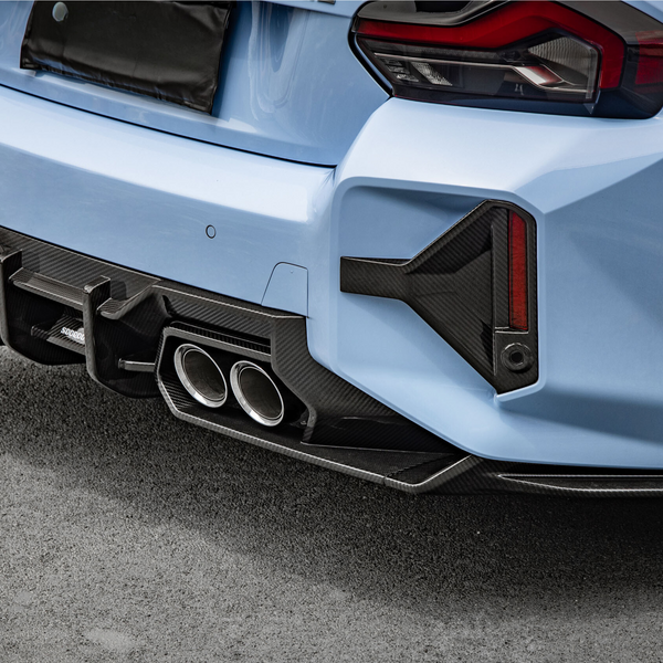 A light blue car with sporty dual exhaust pipes and a carbon fiber diffuser is parked on a paved surface. The rear taillights have an angular design.