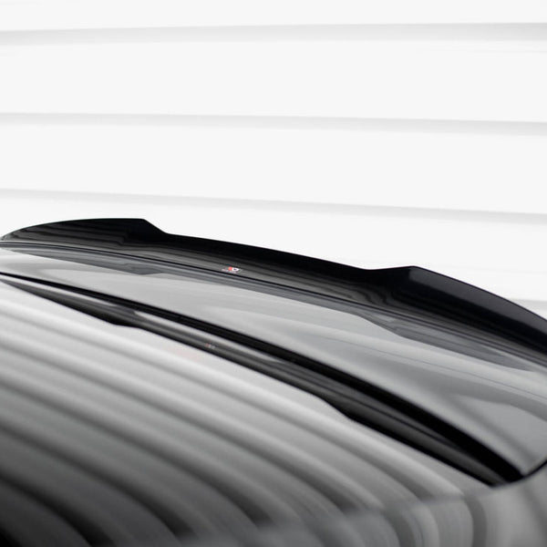 A glossy black car roof with a subtle spoiler reflects light, under a white striped ceiling, creating a sleek, modern appearance.