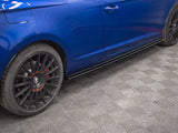 A blue car is parked on a textured gray floor. It features black wheels with red accents, and the side panel is visible with lines reflecting overhead lights.