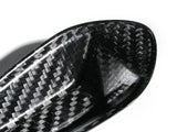 A close-up of a carbon fiber object, possibly a part of sports equipment, displaying a woven pattern. It is set against a plain white background.
