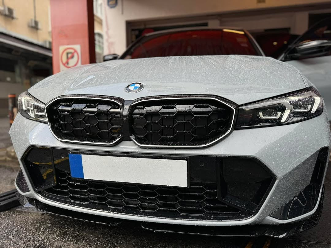 A silver BMW car parked in a garage, its hood covered in raindrops. A no-parking sign is visible on a red post nearby.