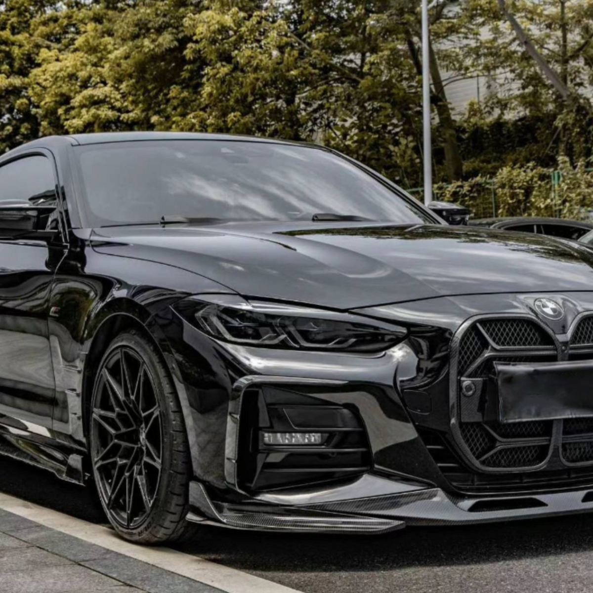A sleek black sports car is parked on a street lined with trees and other vehicles, its glossy surface reflecting the surroundings, emphasizing its modern, aerodynamic design.