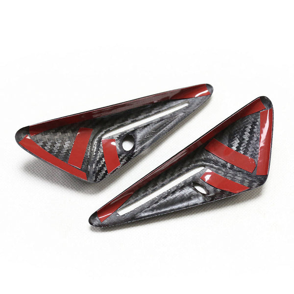 Two black carbon fiber trim pieces with red accents rest on a white surface; each has a small circular hole.