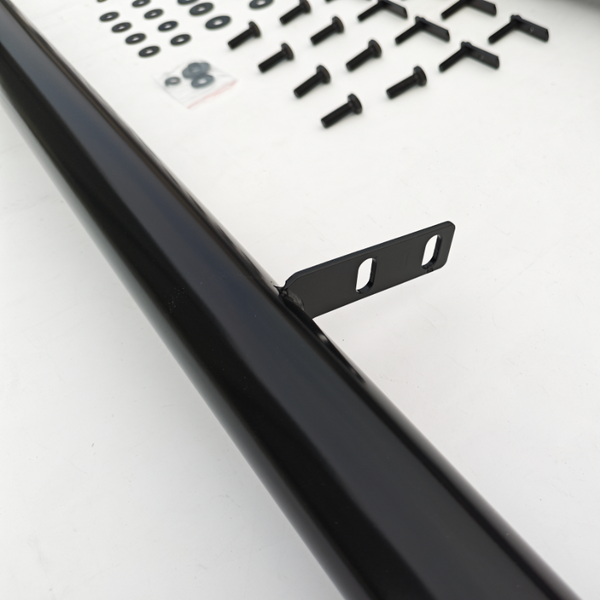 A black metal bar lies on a white surface surrounded by various screws and washers. The bar features a flat metal bracket with two slots, suggesting assembly use.