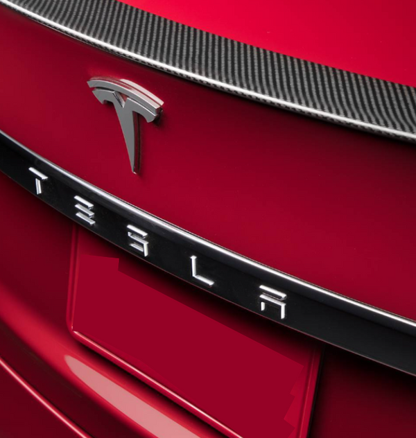A red car features a prominent Tesla emblem and lettering on the rear, with a carbon-fiber trim above.