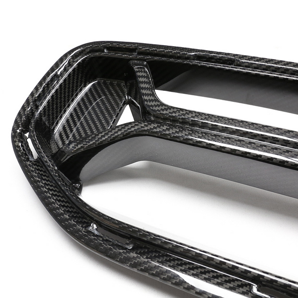 A carbon fiber car grille with a glossy finish, featuring an intricate weave pattern, rests on a plain white surface.