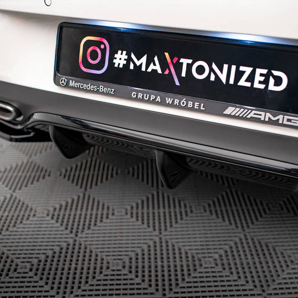 Car rear features a customized license plate with "#MA XTONIZED," Instagram logo, "Mercedes-Benz GRUPA WRÓBEL AMG," above a black bumper and exhausts, parked on a patterned floor.