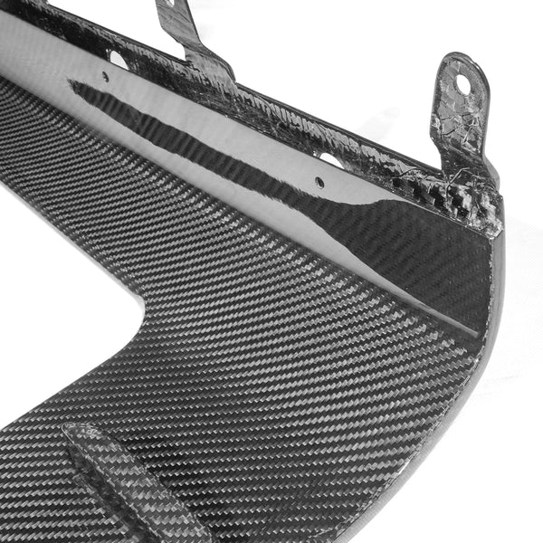 A close-up view of a carbon fiber automotive component with a textured pattern, featuring mounting brackets along the edge, set against a plain background.