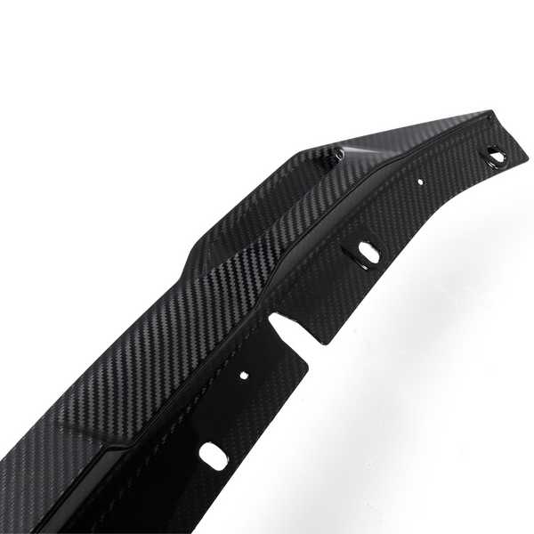 A contoured carbon fiber car part with multiple holes lies against a white background, showcasing a sleek, textured design often used for aerodynamic enhancements.