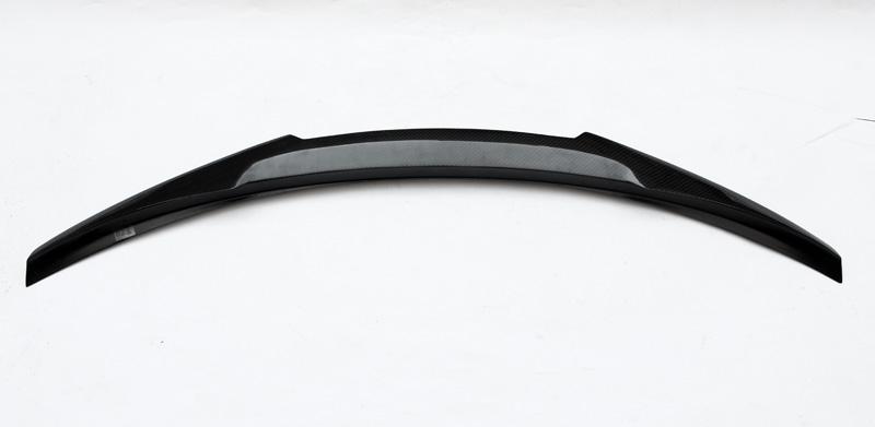 A black, curved car spoiler with a textured surface is positioned against a plain white background, highlighting its aerodynamic design.