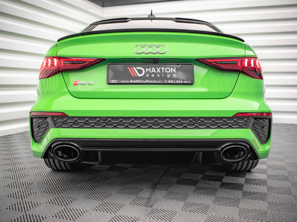 A bright green Audi RS3 is stationary on a checkered floor, viewed from the rear. The car features dual exhausts and a Maxton design plate. Surrounding walls are reflective and angular. Text on the plate reads: "MAXTON design / www.AudiCityPkock.pl / 665 536 800".