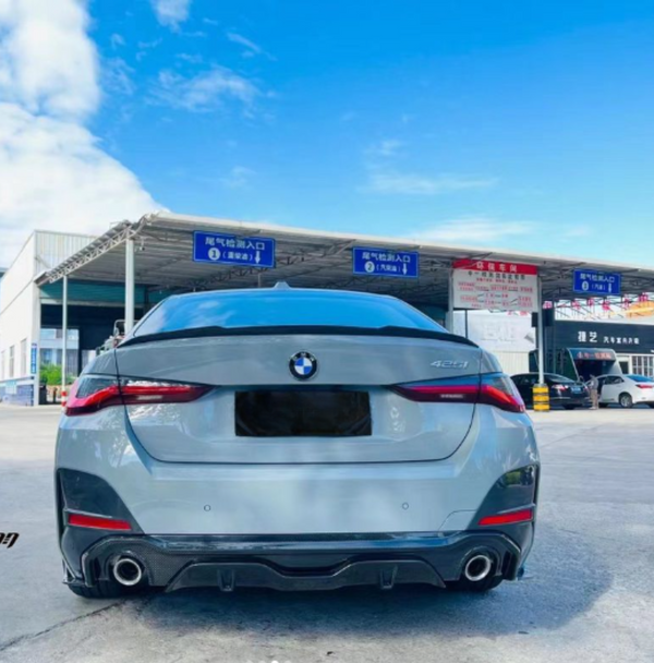 A silver BMW 4-series car is parked in front of an automotive service station. Blue signs in Chinese above indicate the entrance as "尾气检测入口" (Exhaust Inspection Entrance).