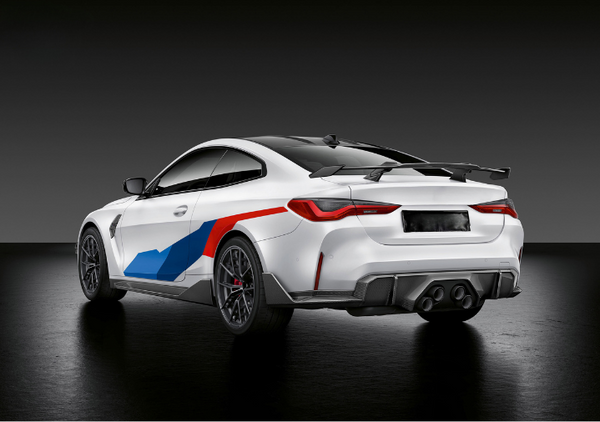 A white sports car with blue and red accents is parked in a dark studio setting. It features a rear spoiler, quad exhaust, and sleek lines highlighting its aerodynamic design.