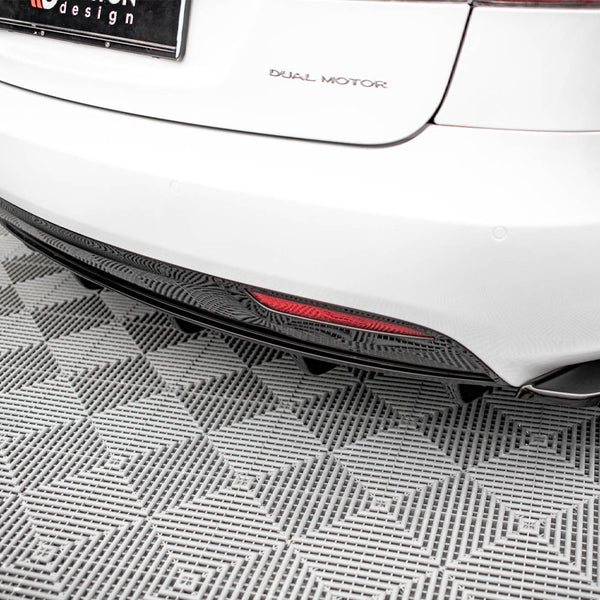 A white car's rear, labeled "DUAL MOTOR," is parked on a gray, textured floor. A red reflector is visible on the lower bumper, and the license plate includes "design."