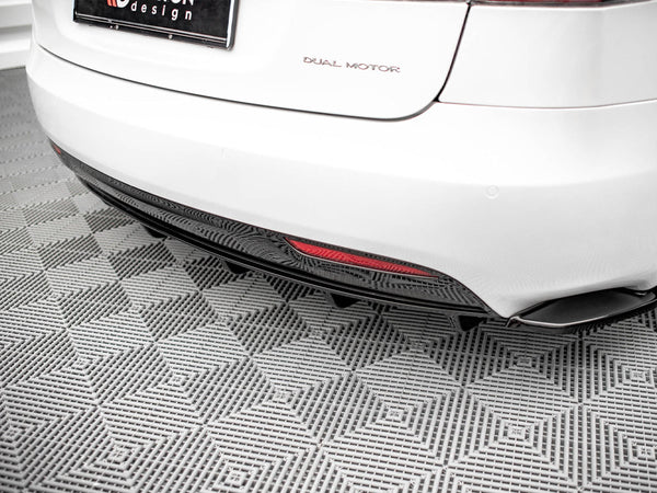 A white car's rear, labeled "DUAL MOTOR," is parked on a gray, textured floor. A red reflector is visible on the lower bumper, and the license plate includes "design."