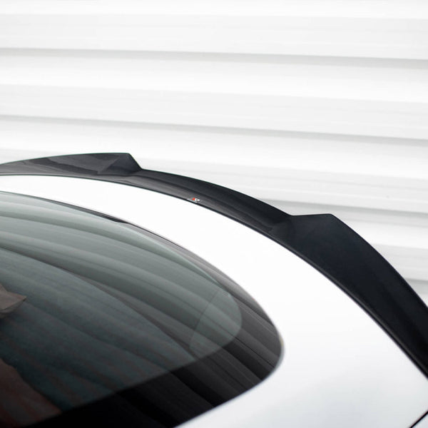 A sleek black car spoiler is mounted on a white vehicle's rear, with a reflective glass surface, set against a striped, white metal background.