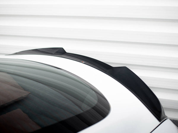 A sleek black car spoiler is mounted on a white vehicle's rear, with a reflective glass surface, set against a striped, white metal background.