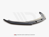 A glossy black car front splitter with aerodynamic fins rests on a white surface. Text reads: 