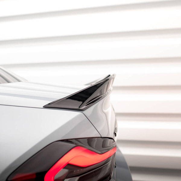 A sleek car's rear, featuring a glossy black spoiler, displays bright red taillights. It is set against a background of evenly spaced horizontal white panels.