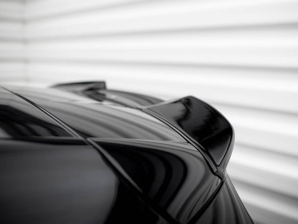 A sleek, black car spoiler is shown from a low angle; the surface reflects light. The background is a blurred, white, horizontal-striped wall.