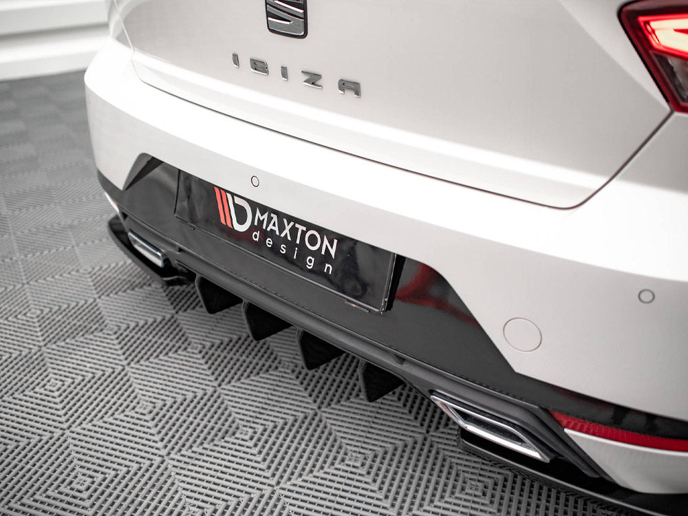 The rear of a white car with the word "IBIZA" and a "MAXTON design" label is parked on a patterned floor, featuring dual exhausts and a textured diffuser.