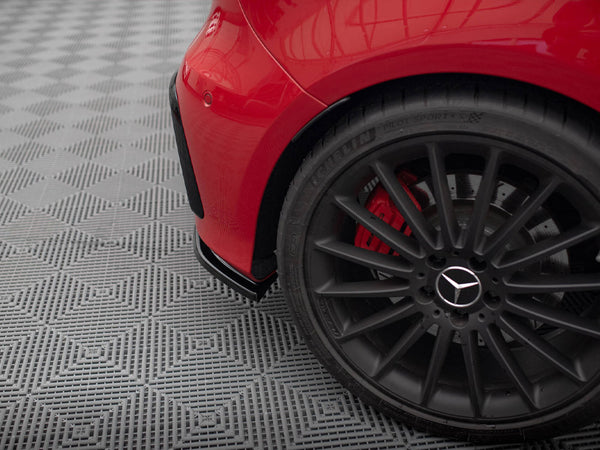 A black alloy wheel with a Mercedes logo is stationary on a patterned gray surface. The car, painted red, is partially visible with a rear fender.