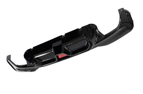 A glossy black car bumper with angular cutouts is isolated on a white background, featuring a central red reflective element.