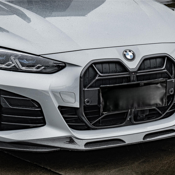 A matte gray BMW car with prominent grille and sleek headlights is parked on a wet, reflective ground surface, surrounded by outlined parking spaces.
