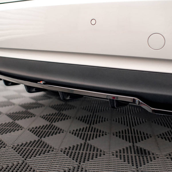 The rear of a white car with parking sensors is displayed, showcasing a black diffuser and exhaust pipes. It is situated on a checkered-patterned floor.
