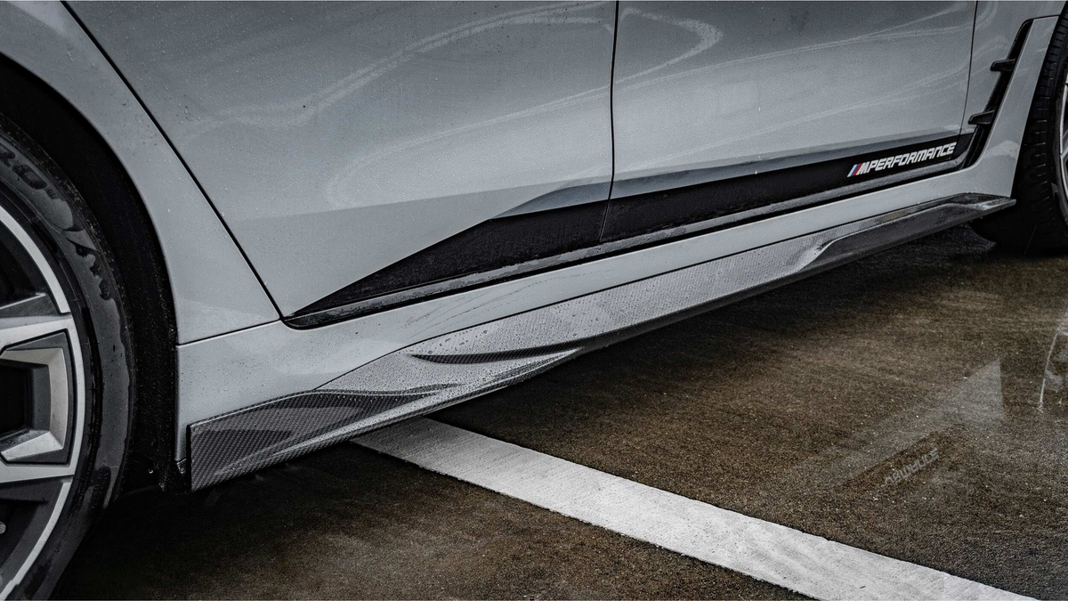 Car side skirt with "M PERFORMANCE" text is enhanced by raindrops. It's part of a sleek vehicle parked on wet pavement with a white painted line.